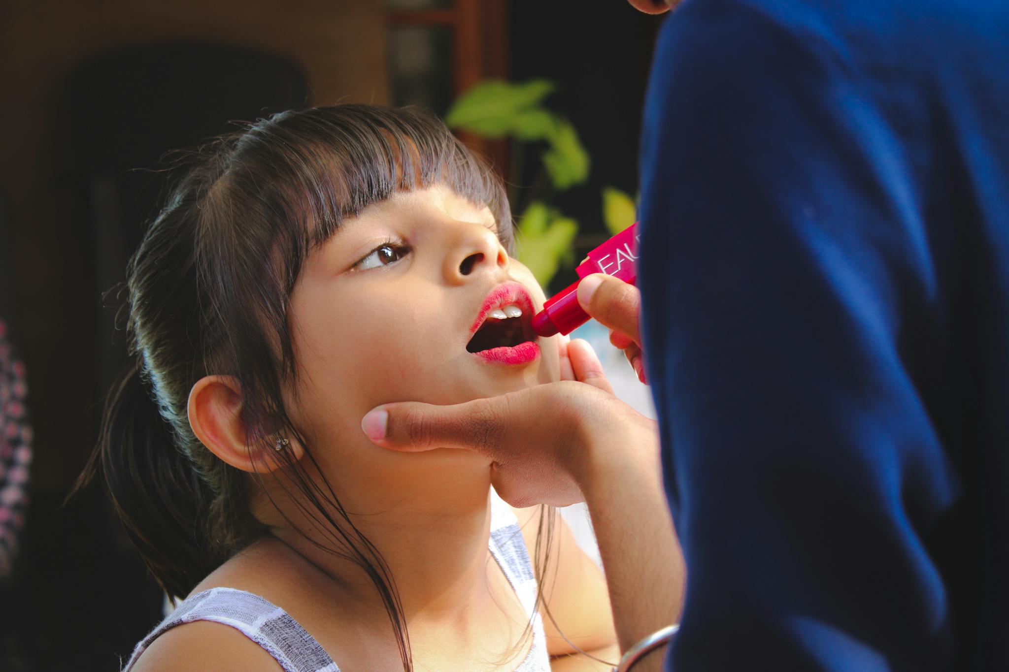 Adorable young girl having lipstick applied. Captures innocence and playfulness.