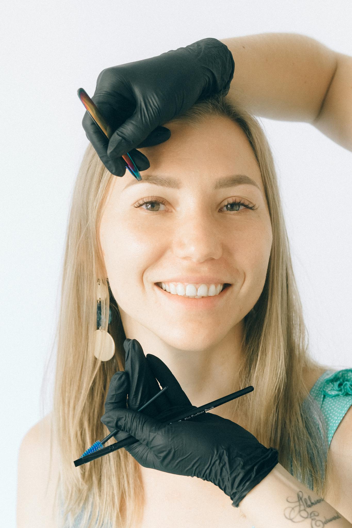 Smiling woman receiving eyebrow microblading treatment in a professional salon setting.